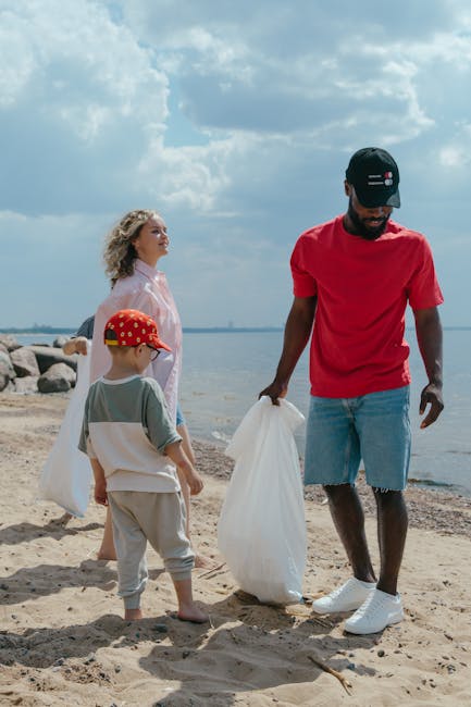 A family engaged in a beach cleanup on a partly cloudy day, with a man wearing a black cap, red t-shirt, and light blue shorts holding a white rubbish bag, while a woman in a light pink cover-up and a young boy in a gray t-shirt, beige shorts, and a red cap with white dots stand nearby. The family is positioned on sandy terrain along a coastline with visible rocks and calm water extending into the distance. The sky features scattered clouds, providing natural daylight that illuminates the scene clearly. This outdoor setting depicts private waste collection efforts, emphasizing responsible disposal of collected litter in a natural environment, which aligns with alternative waste handling practices often supported by waste disposal services like Waste Disposal Enfield.