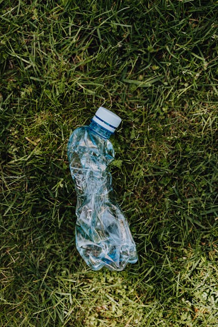 A discarded clear plastic water bottle with a white cap lies on a patch of green grass. The bottle is crumpled and partially flattened, with visible ridges and transparency showing its empty interior. The surrounding grass is lush, with varying shades of green and scattered blades, indicating an outdoor setting such as a lawn or park area. The environment appears natural and undisturbed, with no visible background structures or other debris. This image highlights issues related to littering and improper waste disposal, which are relevant to independent rubbish removal services like Waste Disposal Enfield that offer alternative waste handling options outside of municipal collection. The scene emphasizes the importance of responsible waste management and keeping outdoor spaces clean from single-use plastic litter.